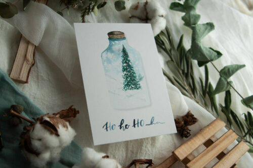 Weihnachtspostkarte „HO HO HO“ zeigt eine handgezeichnete Illustration eines festlichen Tannenbaums in einer Glasflasche, umgeben von einer winterlichen Schneelandschaft. Gestaltet von Frau Feierlich