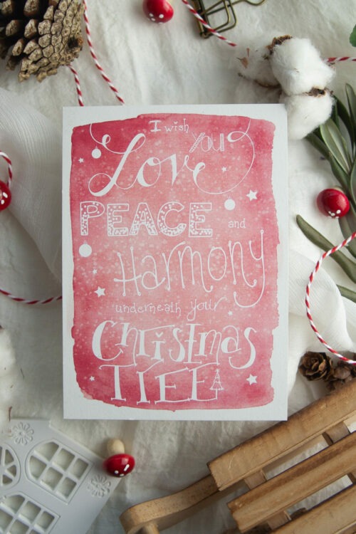 Weihnachtspostkarte "love Peace Harmony" mit handgezeichneter Typografie und der Botschaft "I wish you Love, Peace, and Harmony underneath your Christmas Tree" auf rotem Hintergrund, gedruckt auf umweltfreundlichem Recyclingpapier. Gestaltet von Frau Feierlich
