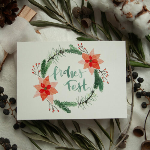Weihnachtspostkarte im A6-Format mit handgemaltem Aquarell-Kranz aus Tannenzweigen, roten Weihnachtssternen und Beeren. In der Mitte steht der Schriftzug „Frohes Fest“. Die Karte ist auf hochwertigem Recyclingkarton gedruckt und ideal für nachhaltige Weihnachtsgrüße. Gestaltet von Frau Feierlich