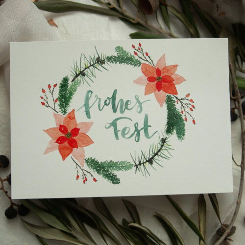 Weihnachtspostkarte im A6-Format mit handgemaltem Aquarell-Kranz aus Tannenzweigen, roten Weihnachtssternen und Beeren. In der Mitte steht der Schriftzug „Frohes Fest“. Die Karte ist auf hochwertigem Recyclingkarton gedruckt und ideal für nachhaltige Weihnachtsgrüße. Gestaltet von Frau Feierlich