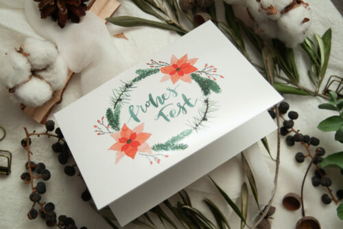 Weihnachtspostkarte | Klappkarte im A6-Format mit handgemaltem Aquarell-Kranz aus Tannenzweigen, roten Weihnachtssternen und Beeren. In der Mitte steht der Schriftzug „Frohes Fest“. Die Karte ist auf hochwertigem Recyclingkarton gedruckt und ideal für nachhaltige Weihnachtsgrüße. Gestaltet von Frau Feierlich